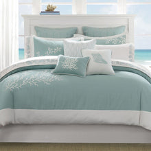 Load image into Gallery viewer, A queen-sized bed with a Harbor House Coastline comforter set, featuring intricate coral and shell embroidery on the bedding. The bed is placed in a room with a coastal theme and ocean view.